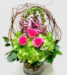 three pink roses with green hydrangea and lavender floral accents in basket