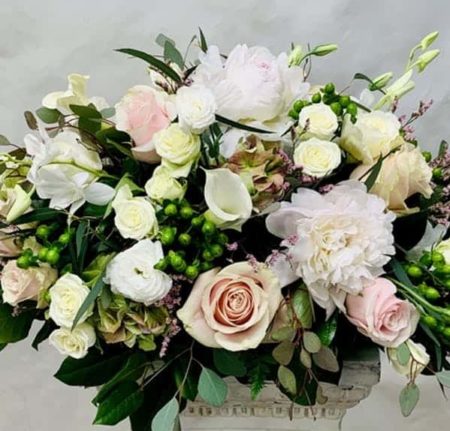 White peonies, peach and yellow roses with greens in a vase