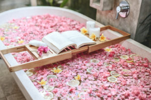 Bathtub with pink flower petals, fruit, candles, and open book